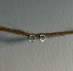 Two silver hoop earrings on a string against a plain background