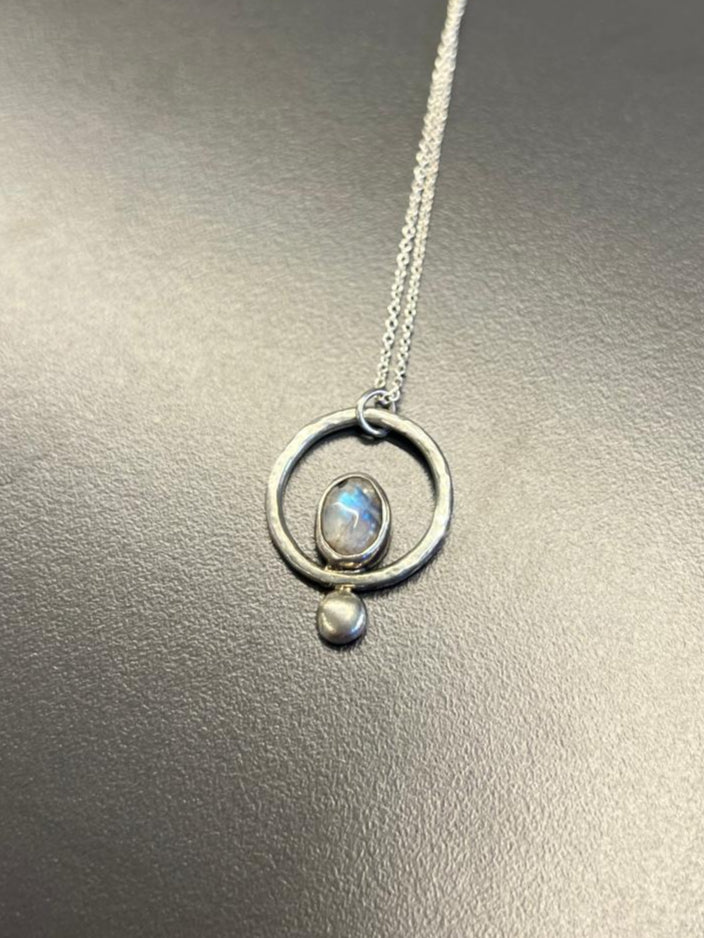 Silver necklace with a circular pendant on a reflective surface