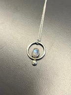 Silver necklace with a circular pendant on a reflective surface